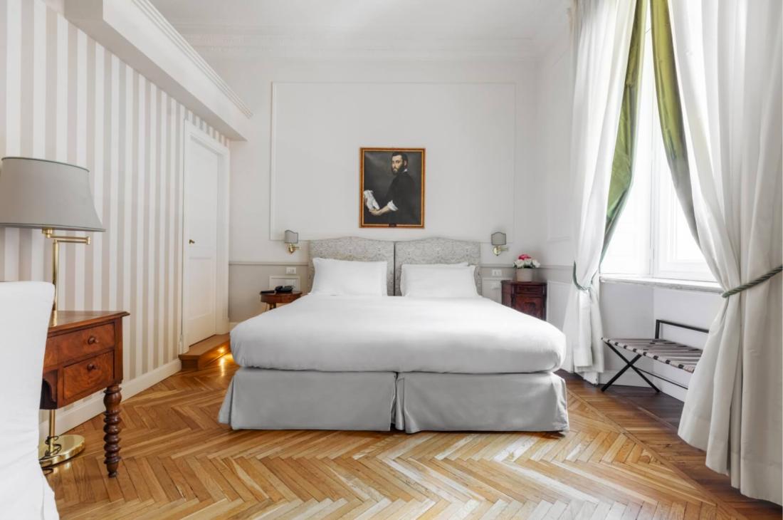 Camera elegante con letto bianco, pavimento in legno, arte classica e luce soffusa.