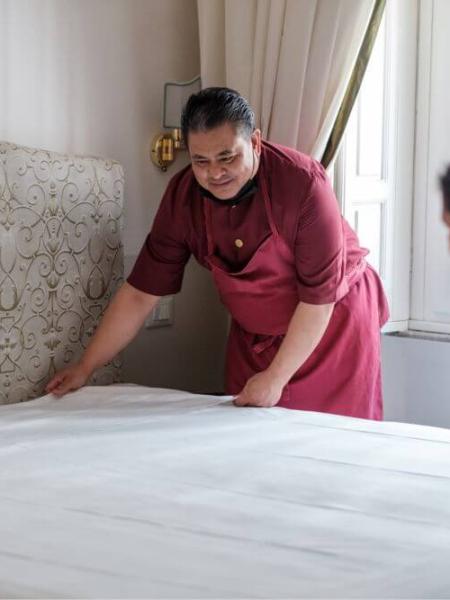 Due persone sorridenti rifanno un letto in una stanza luminosa.