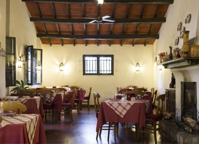 Ristorante rustico con tavoli apparecchiati, camino e atmosfera accogliente.