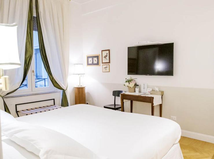 Camera accogliente, elegante, con letto bianco, tende verdi e quadro antico.