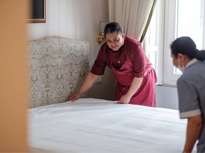 Due persone sorridenti rifanno un letto in una stanza luminosa.