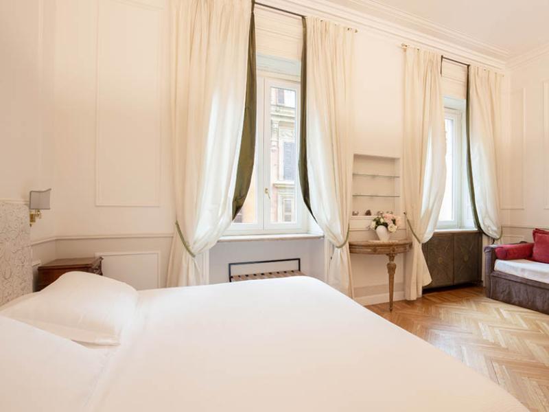 Camera luminosa ed elegante con letto bianco, tende leggere e pavimento in legno.