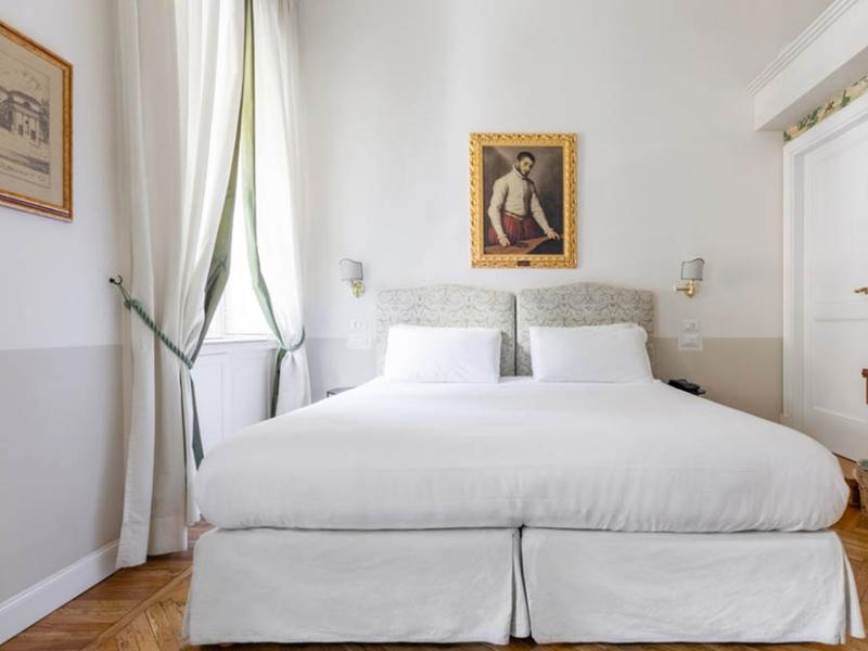 Camera elegante con letto bianco, quadro antico e atmosfera accogliente.