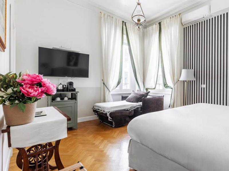 Camera elegante con letto bianco, tende leggere e fiori rosa vibranti.