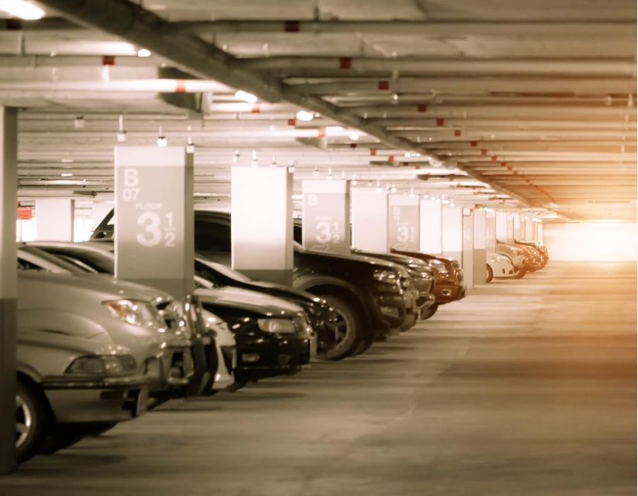 Parcheggio sotterraneo silenzioso, auto allineate, luce calda e sfumata in lontananza.